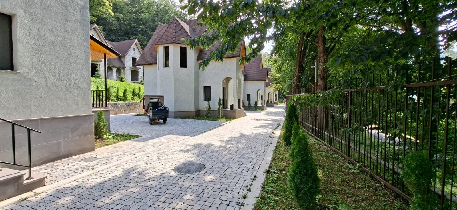 Ein gepflasterter Weg führt an einer Reihe von Häusern vorbei, vor denen Autos geparkt sind.