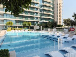 A swimming pool with lounge chairs, surrounded by a modern building with multiple balconies. - Chic full Dubai Marina View 1 BR apartment in LIV Marina (Dubai)