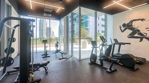 Ein Fitnessstudio mit Trainingsgeräten, großen Fenstern und Blick auf die Stadt.