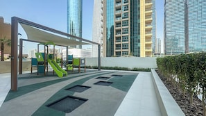 A children's play area with a slide and climbing structures, surrounded by a modern building with reflective glass windows. - Chic full Dubai Marina View 1 BR apartment in LIV Marina (Dubai)