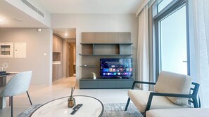 Ein modernes Wohnzimmer mit einem Flachbildfernseher, zwei Sesseln, einem Couchtisch und einem großen Fenster.