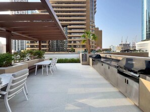 An outdoor patio with a barbecue grill, seating area, and a view of high-rise buildings. - Chic full Dubai Marina View 1 BR apartment in LIV Marina (Dubai)