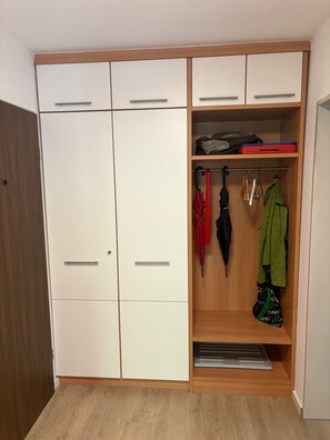 Um closet amplo com piso de madeira, armários brancos para guardar objetos e um cabideiro com diversos itens.