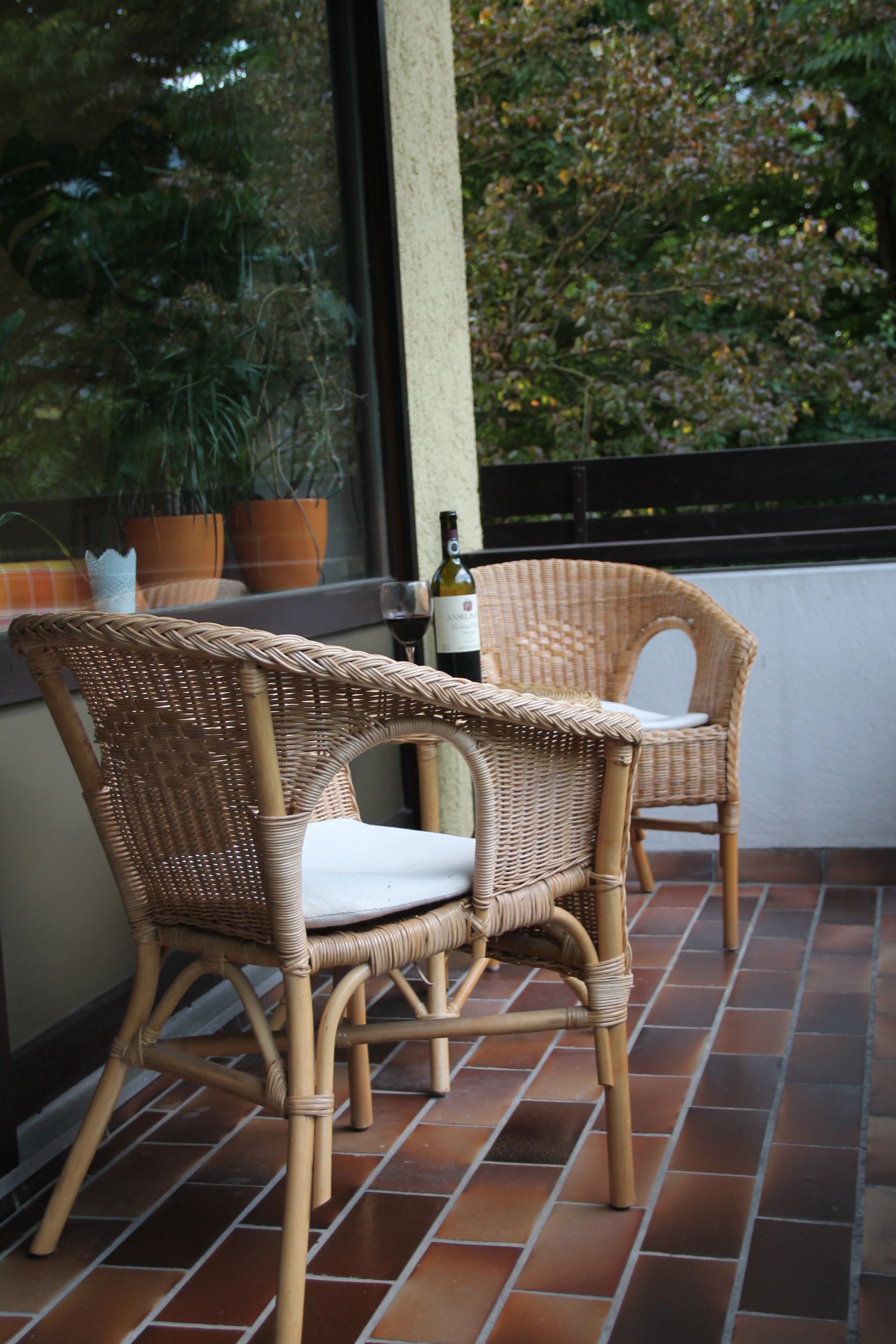 Dos sillas de mimbre con cojines en un patio empedrado.