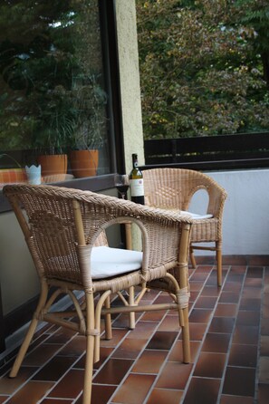 Twee rieten stoelen met kussens op een betegeld terras.