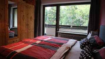 Un dormitorio con cama, un armario de madera, un ventanal con vistas a árboles y un radiador.