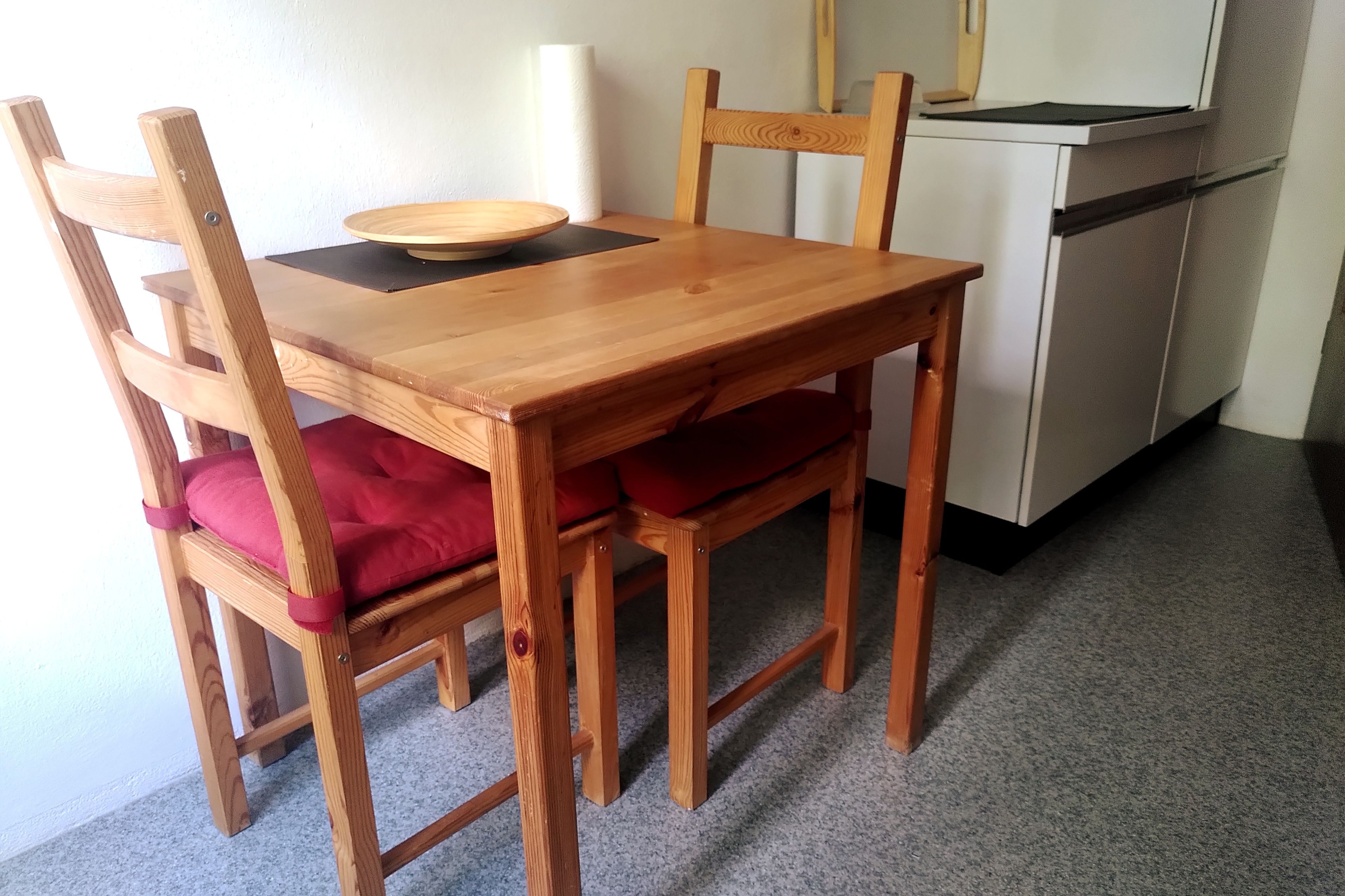 Ein Holztisch mit vier Stühlen, einer Schüssel und einem weißen Gerät im Hintergrund.