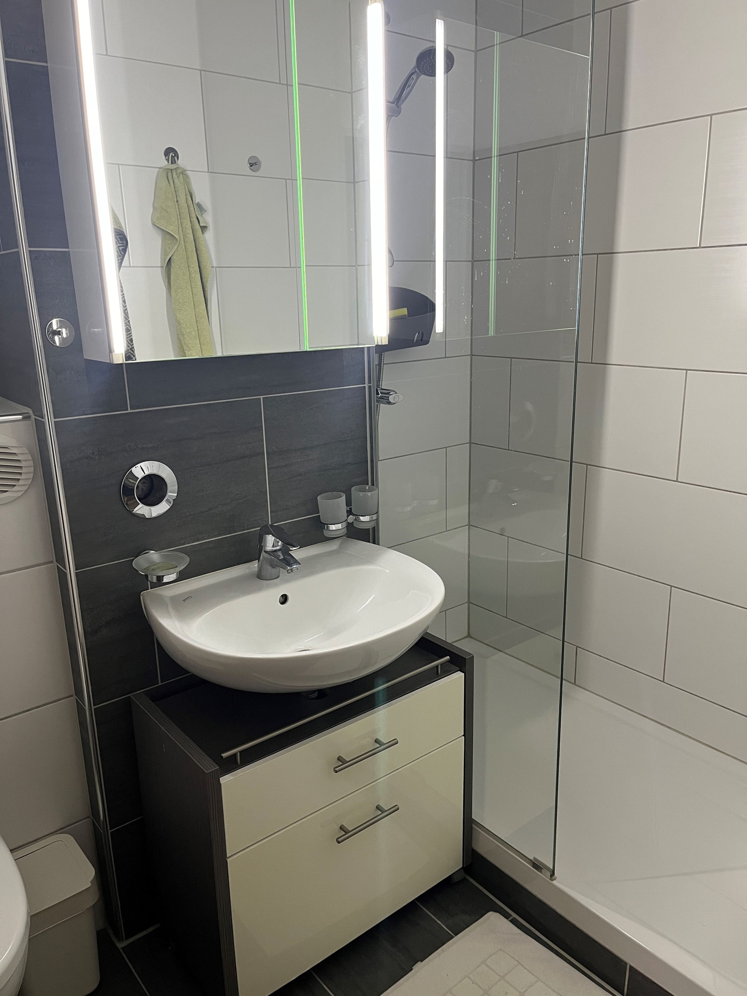 Une salle de bain moderne avec un lavabo blanc, un miroir et une cabine de douche en verre.