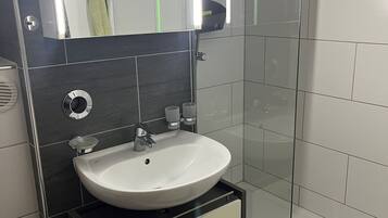 Une salle de bain moderne avec un lavabo blanc, un miroir et une cabine de douche en verre.