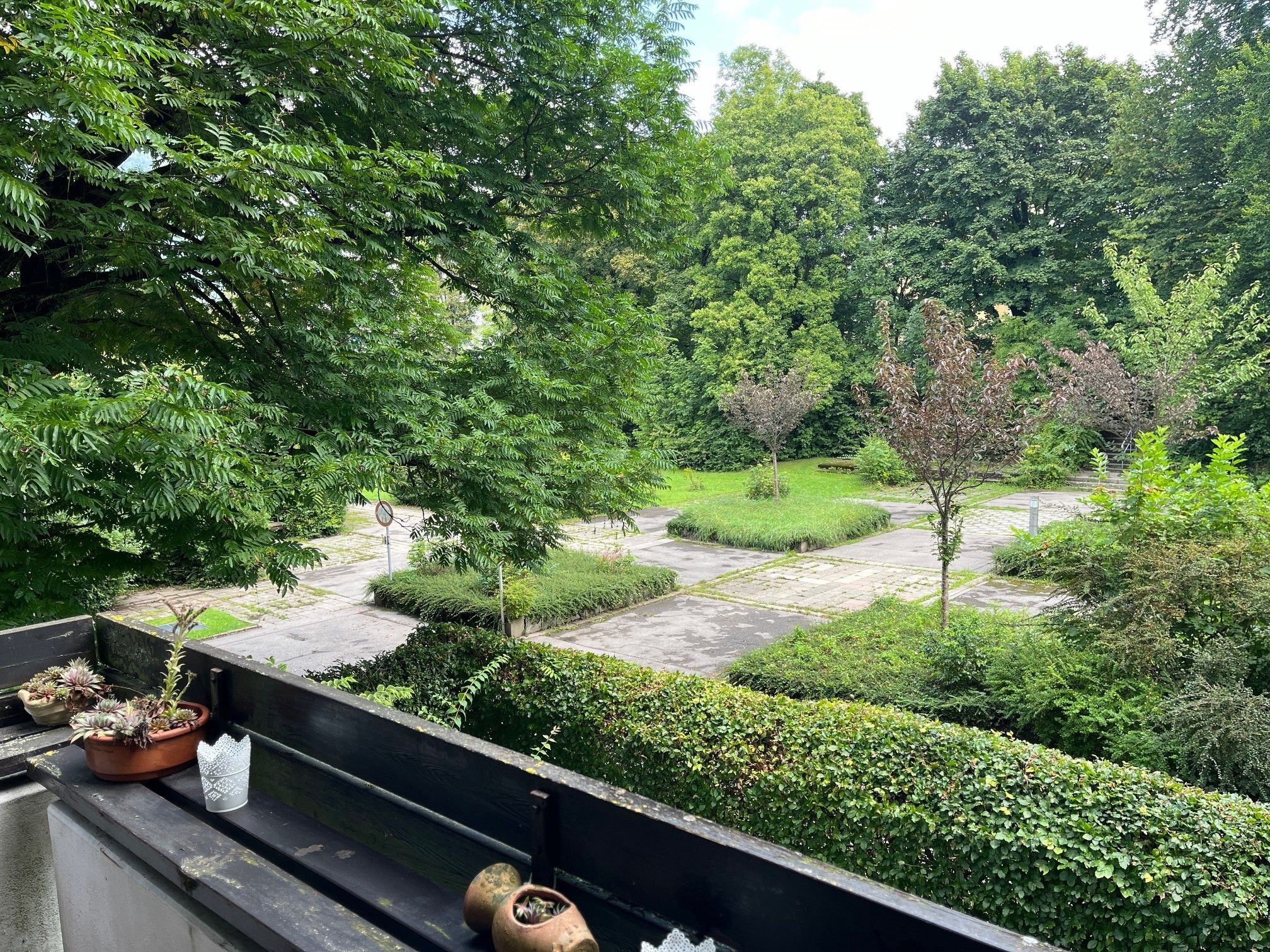 Ein Balkon mit Blumentöpfen, Blick auf einen angelegten Garten mit einem Weg und ein Verbotsschild.