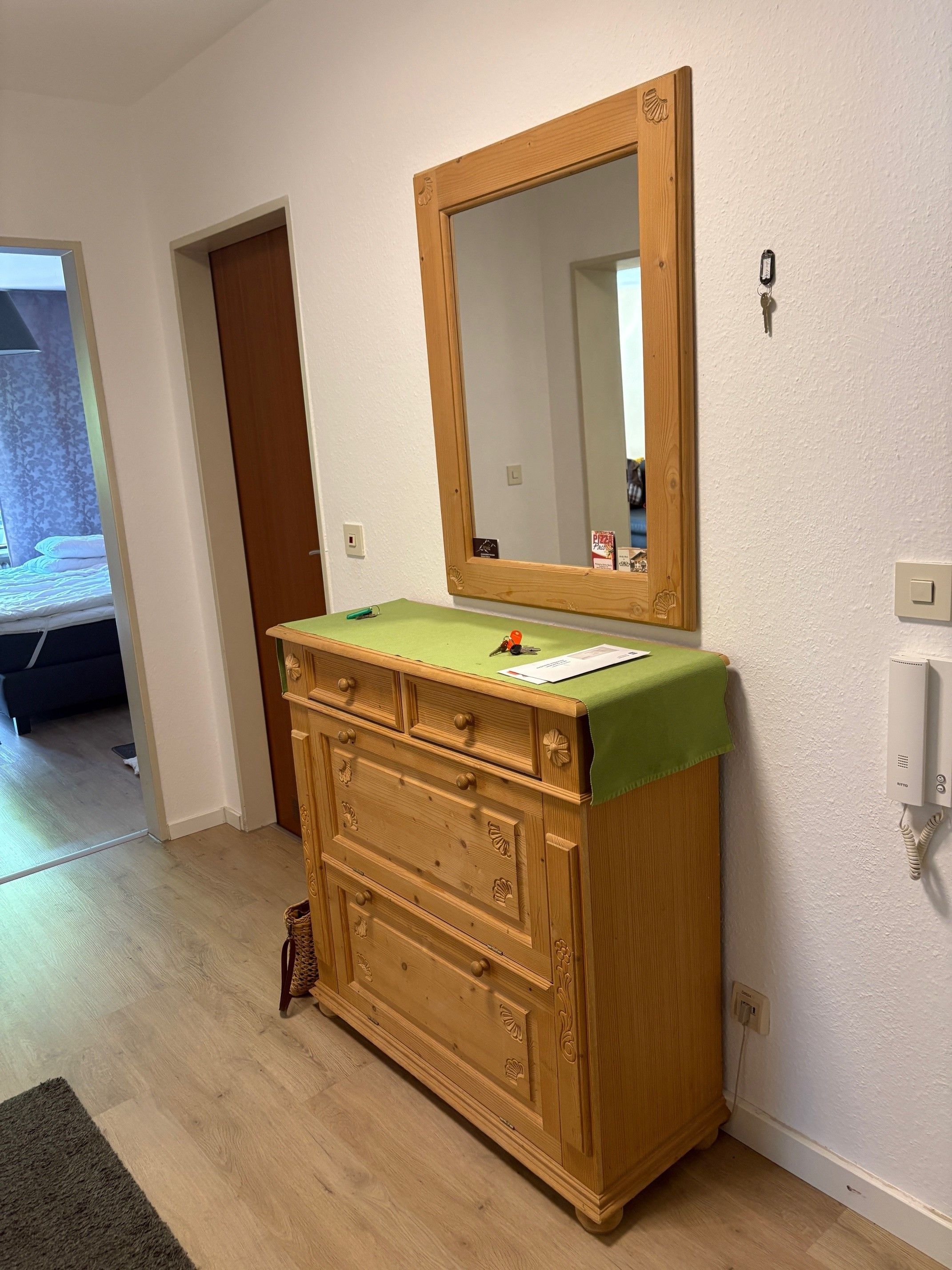 Ein Holzkleiderschrank mit Spiegel, einem grünen Tuch und einem Schlüsselanhänger.