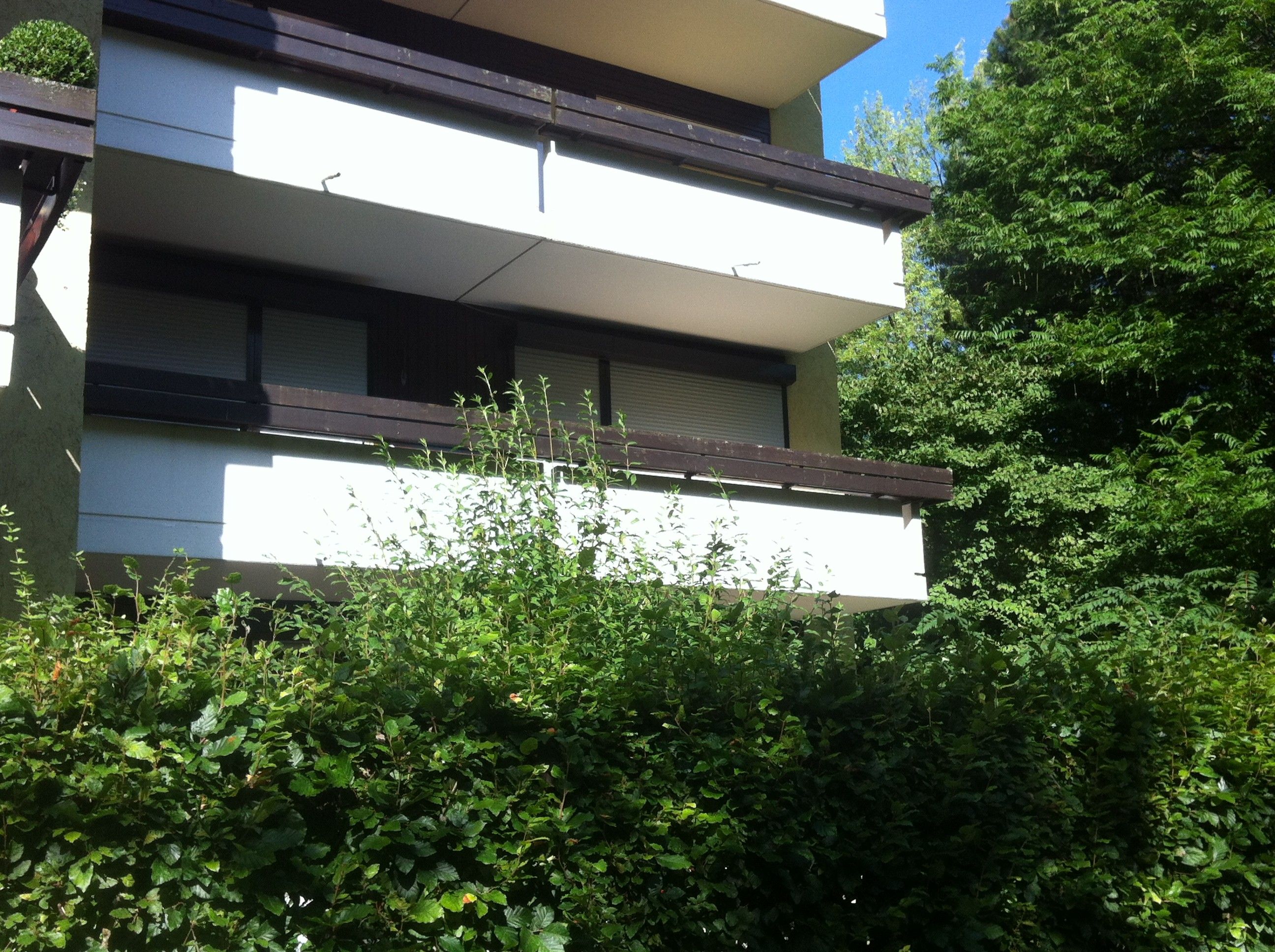 Ein mehrstöckiges Gebäude mit Balkon, umgeben von üppiger Vegetation.