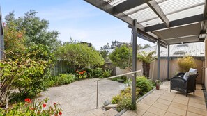 A covered patio with a gravel area, surrounded by lush greenery and a wooden fence. - Quat Quatta - Point Lonsdale (Point Lonsdale)