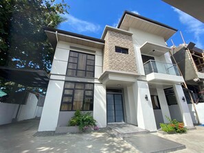 A modern two-story house with a balcony, large windows, and a stone facade.