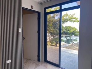 A room with a large sliding glass door leading to an outdoor area with a view of trees and a beach.