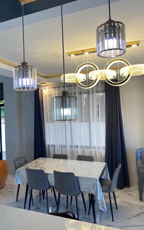 Een eetgedeelte met een tafel voor vier personen, omringd door stoelen, onder een kroonluchter met meerdere lampen.