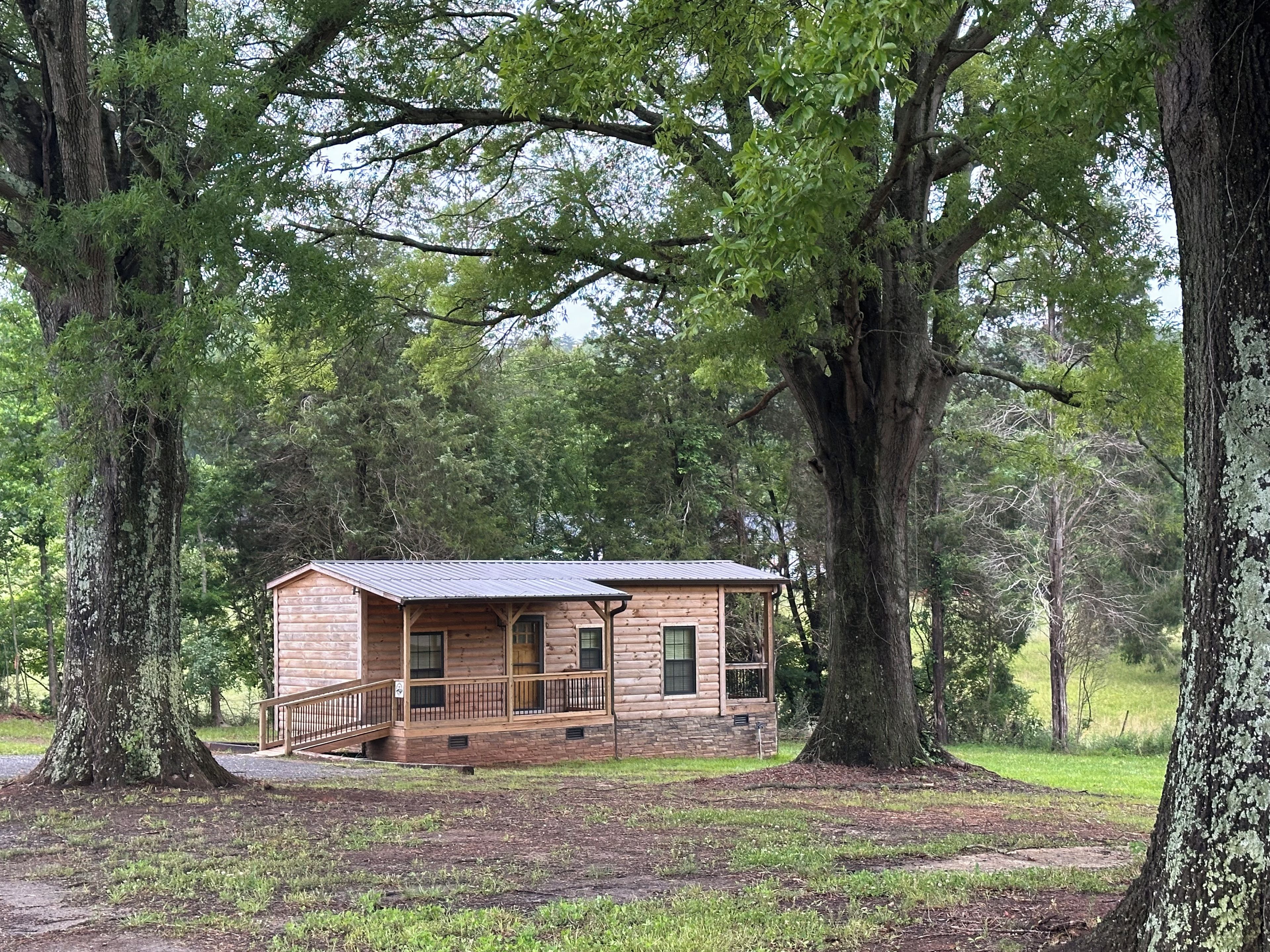 A log cabin with a porch, surrounded by large trees.
