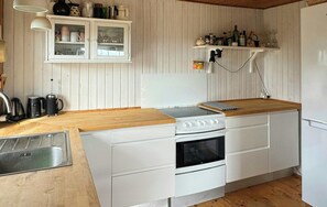 Une cuisine de taille réduite avec des meubles blancs, un plan de travail en bois, une cuisinière, un four et un évier.