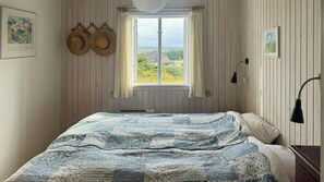 Een slaapkamer met een bed, een raam met gordijnen, een wandlamp en twee hoeden die aan de muur hangen.