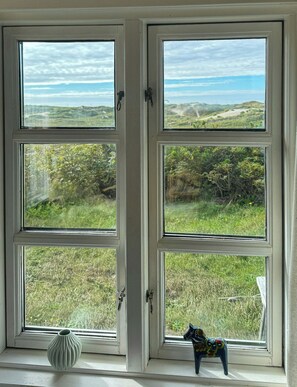 A window with a view of a grassy field and distant hills. - Family summer house on the dune with sea views (Ringkøbing)