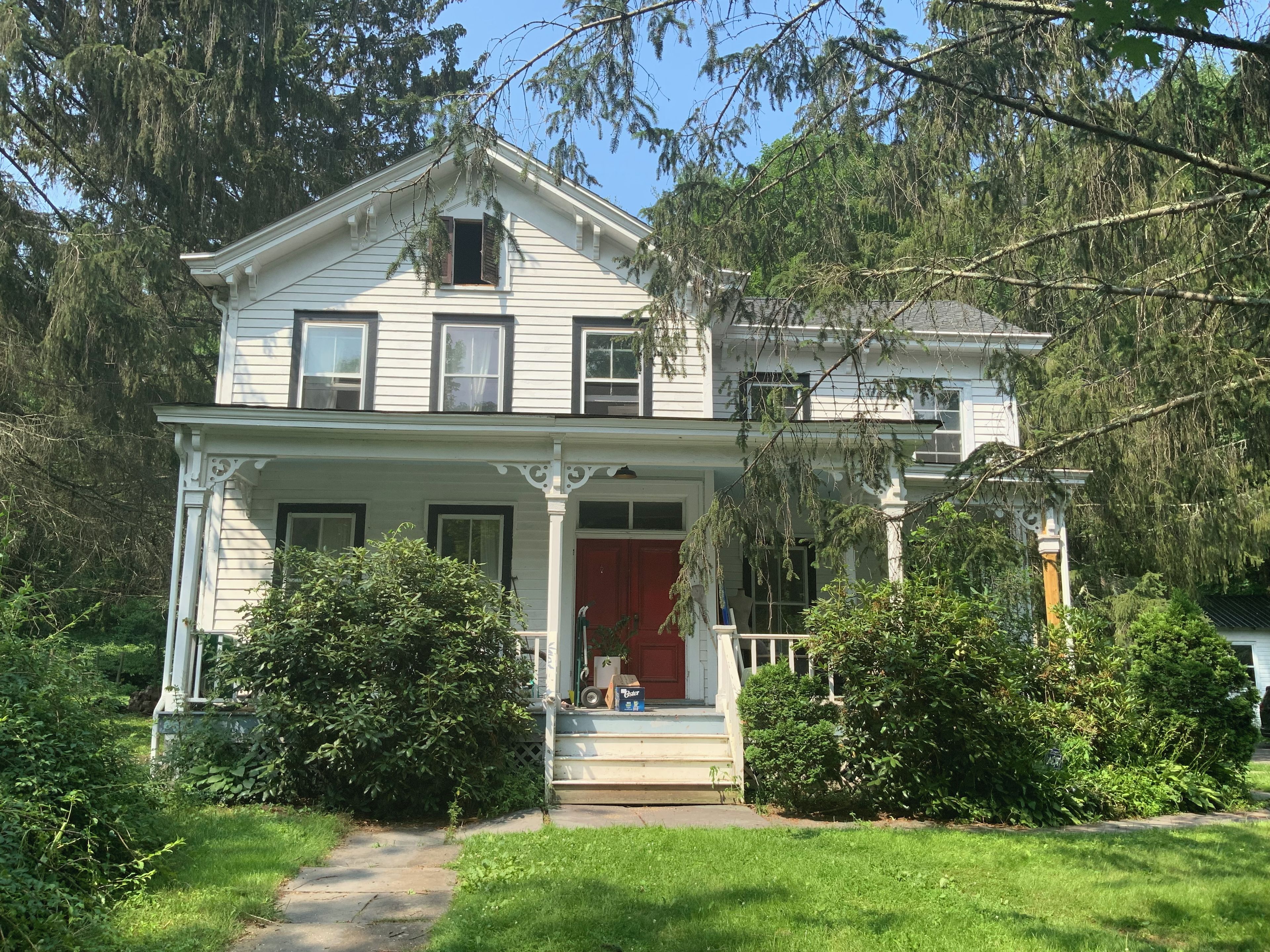 A two-story house with a front porch, a red door, and a small front yard.