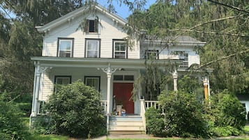 A two-story house with a front porch, a red door, and a small front yard.