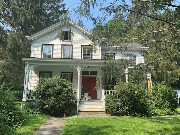 A two-story house with a front porch, a red door, and a small front yard.