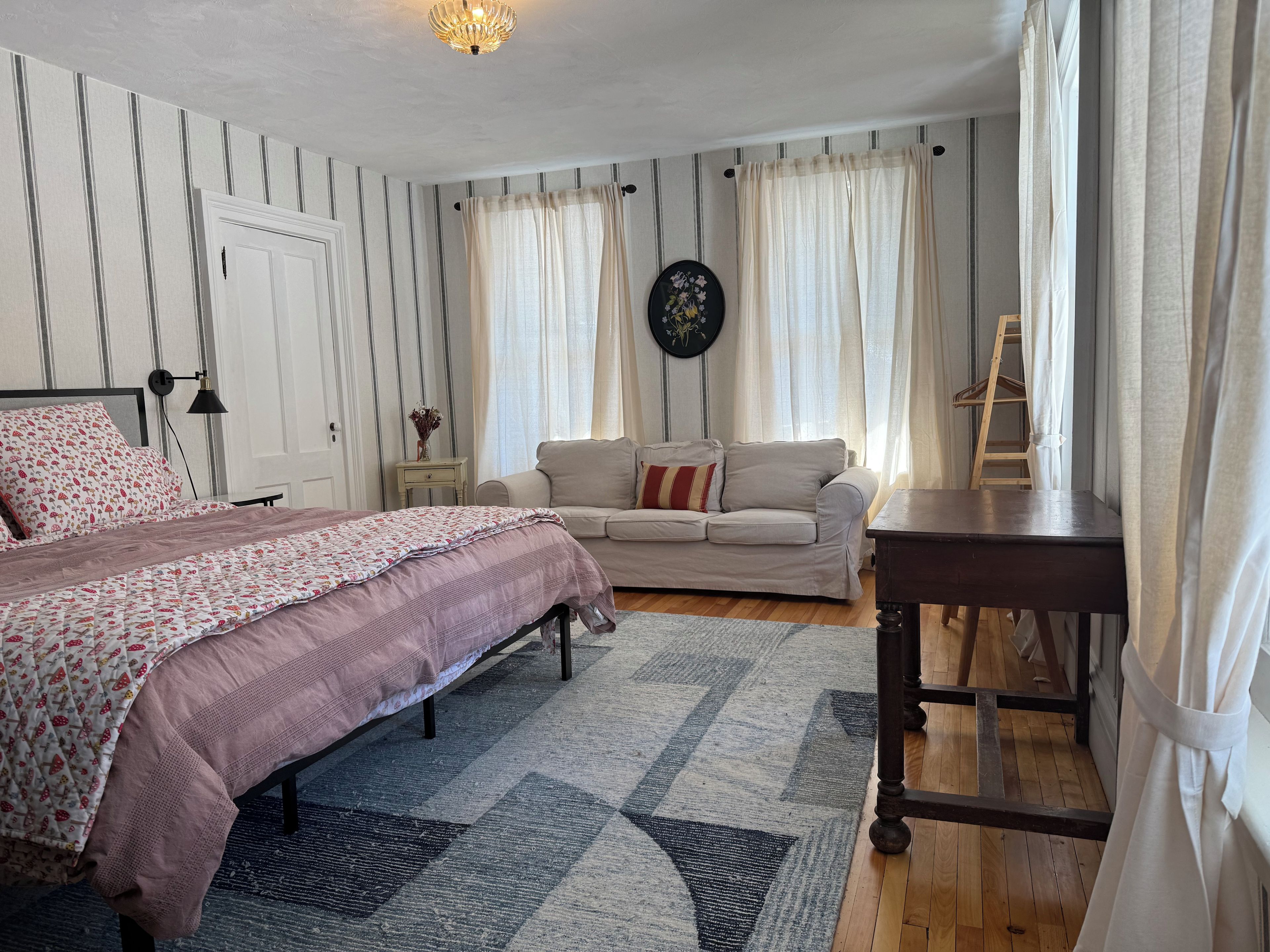 A bedroom with a bed, a sofa, a small table, and a ladder.