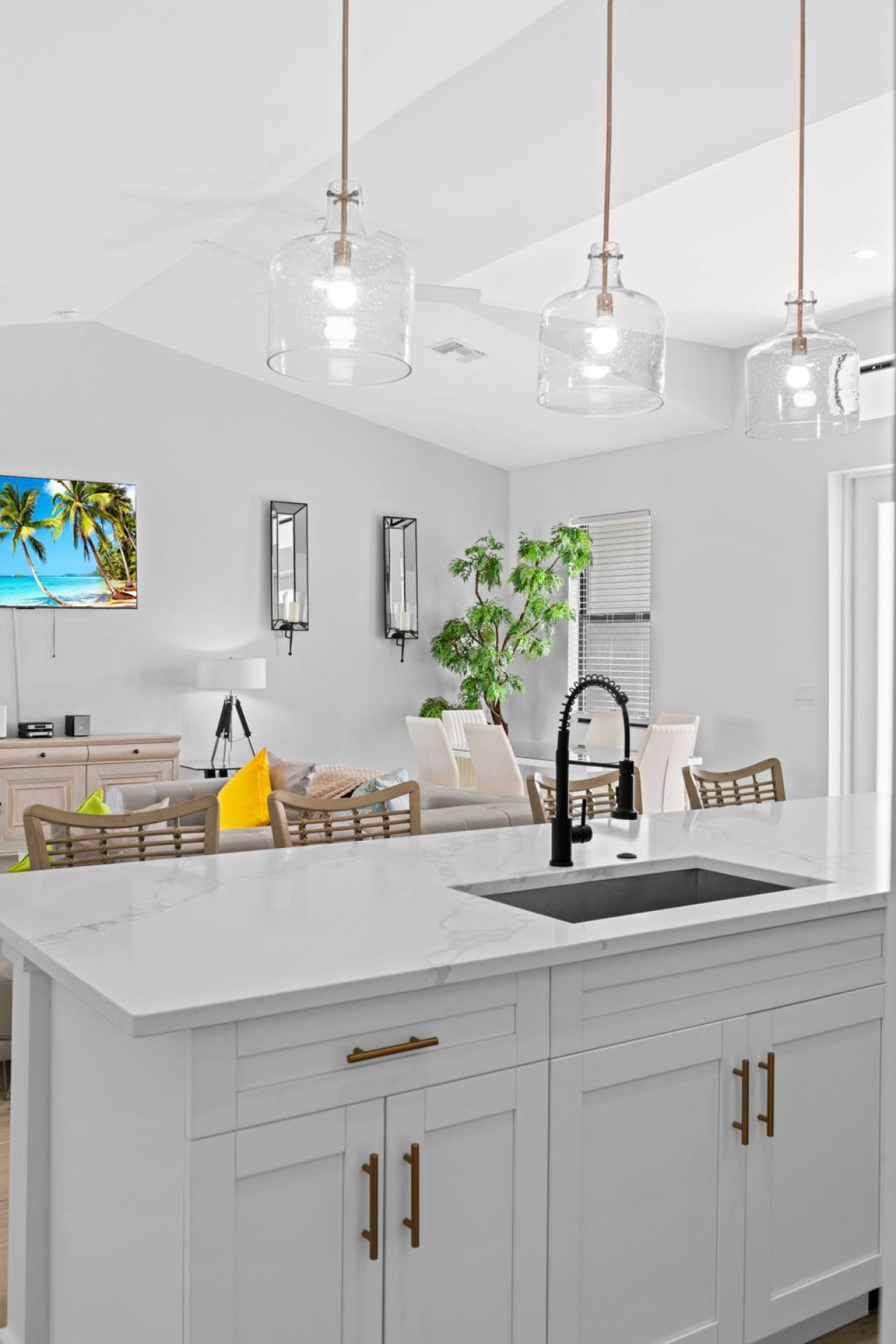 A modern kitchen with a central island, pendant lights, and a view of the living room.