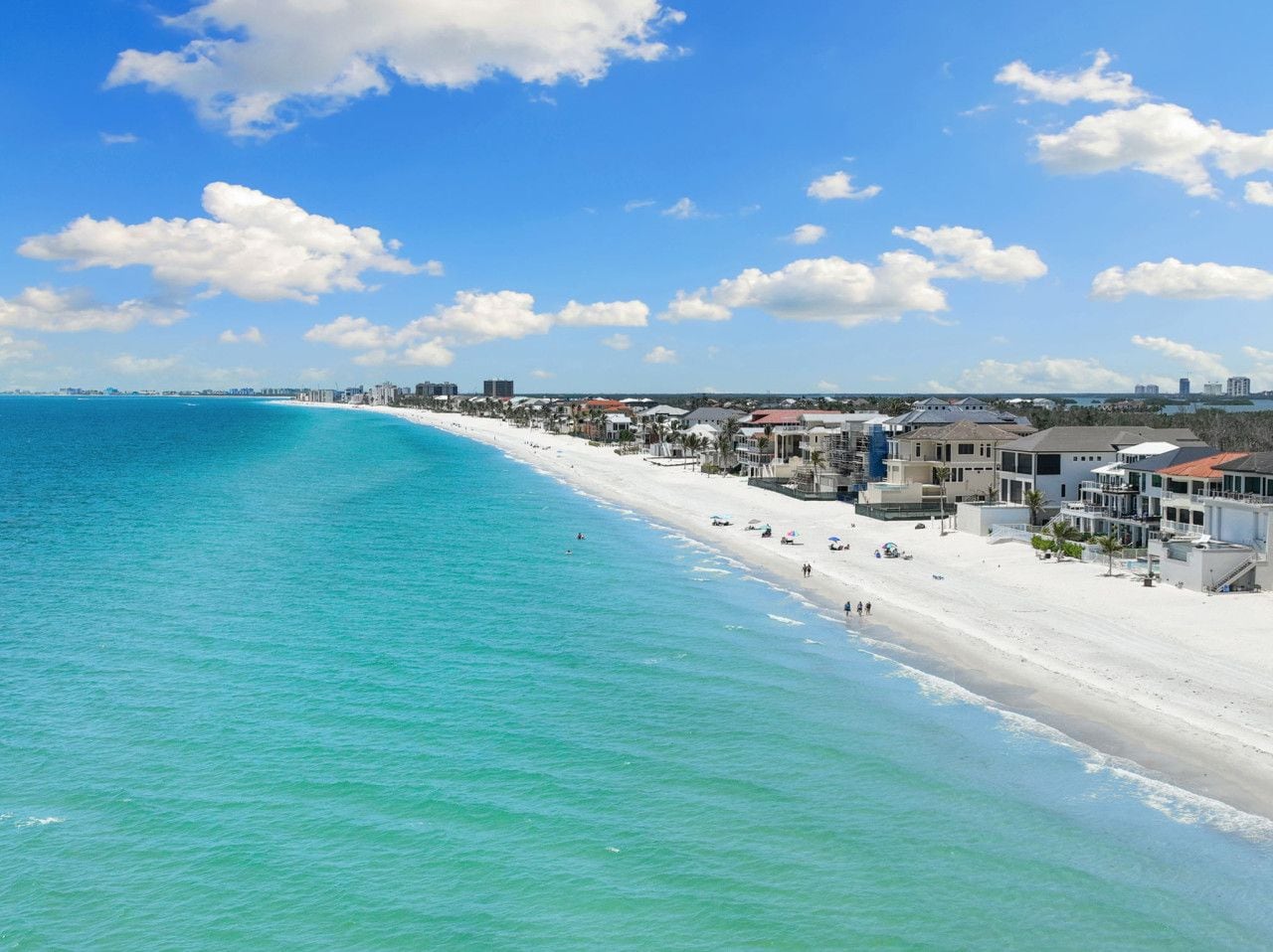 A coastal beach scene with a clear sky, a sandy shoreline, and buildings along the beach.