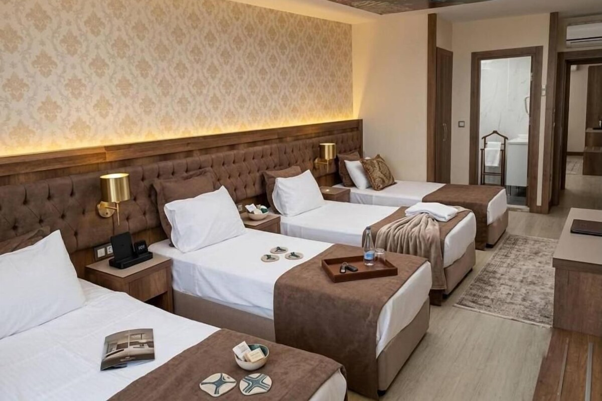 Una habitación de hotel con tres camas, un cabecero de madera, un papel tapiz estampado y un mural en el techo.