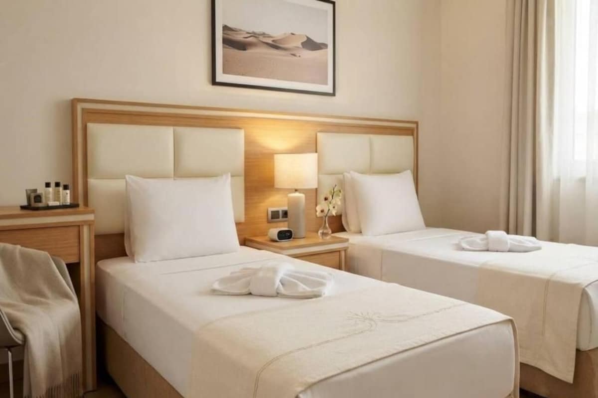 Una habitación de hotel con dos camas, una mesita de noche con lámpara y un cuadro enmarcado en la pared.