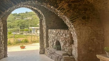 An arched stone structure with a brick floor, a fireplace, and a view of a green landscape.