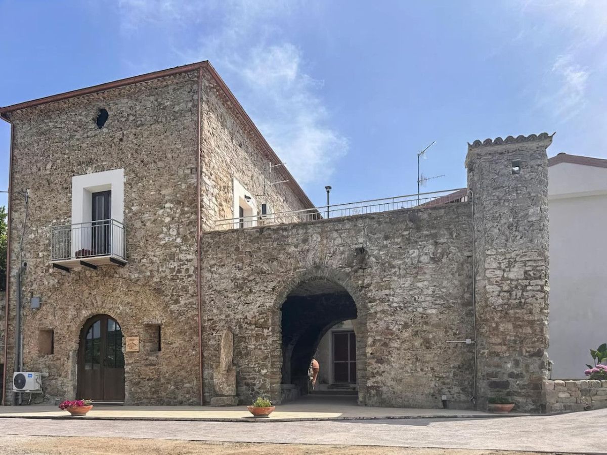 A stone building with a balcony, an arched entrance, and a small tower.