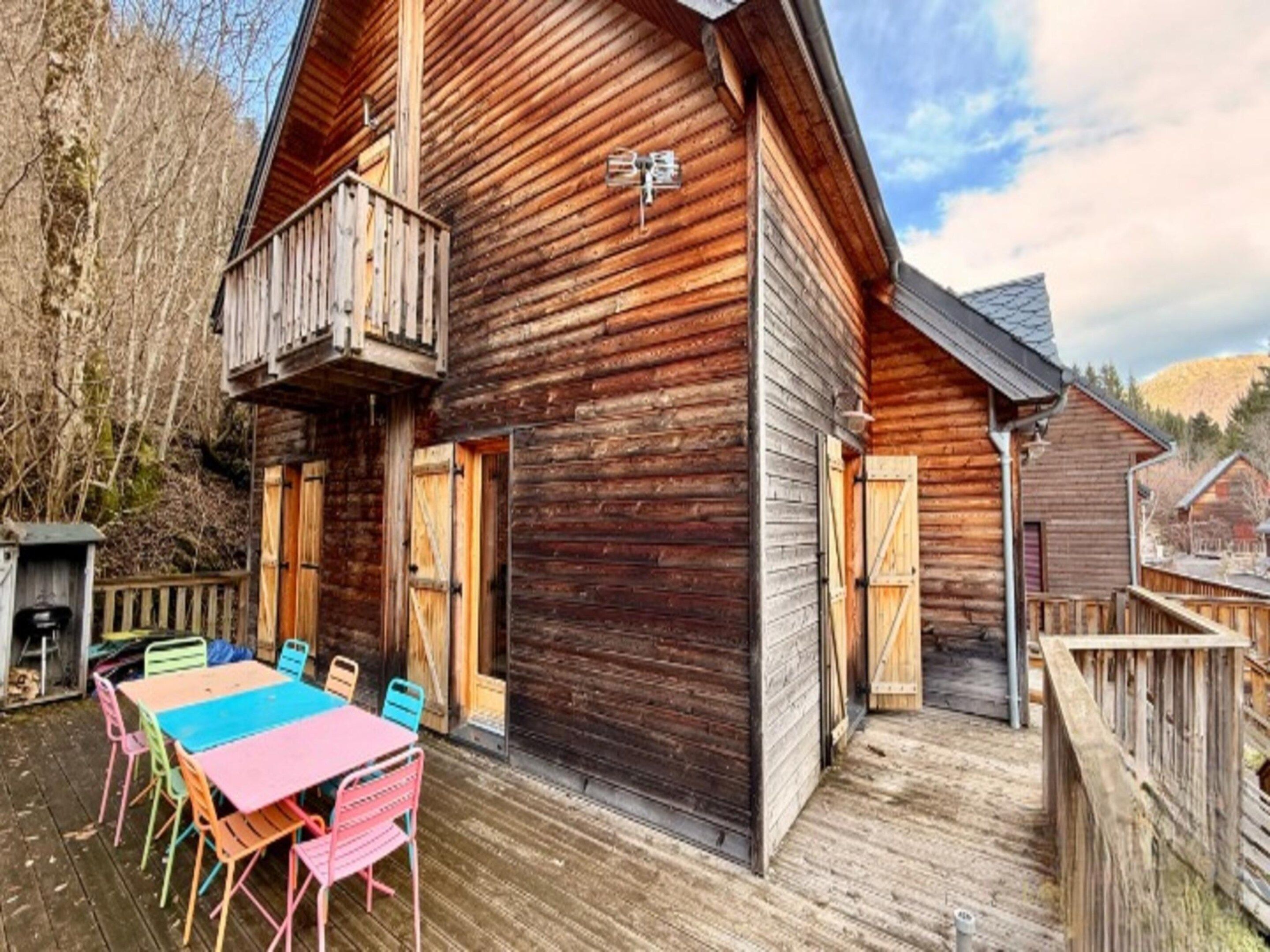 A wooden cabin with a balcony, a deck with colorful chairs, and a rustic exterior.