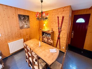 A wooden-paneled room with a dining table, chairs, a chandelier, a coat rack with skis, a door with a window, and a radiator. - Family Chalet With Fireplace, Mont-dore (Mont-Dore)