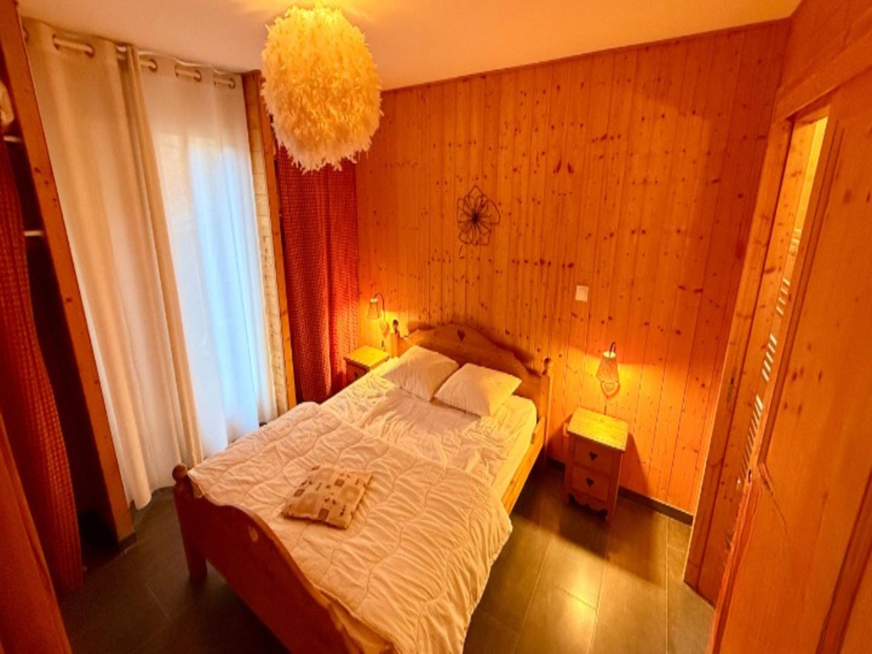 A bedroom with a wooden headboard, a bed with white bedding, two bedside tables with lamps, and a hanging light fixture.