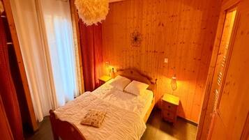 A bedroom with a wooden headboard, a bed with white bedding, two bedside tables with lamps, and a hanging light fixture.