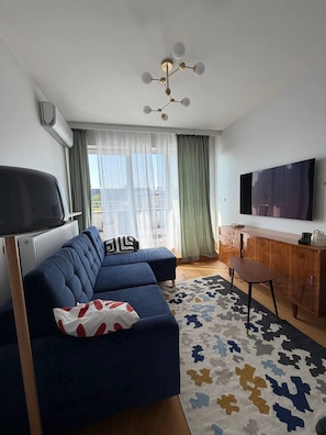 A modern living room with a blue sofa, a wooden cabinet, a television, and a patterned rug. - Lumina 2BR Apt w/ Terrace & Parking (Warszawa)