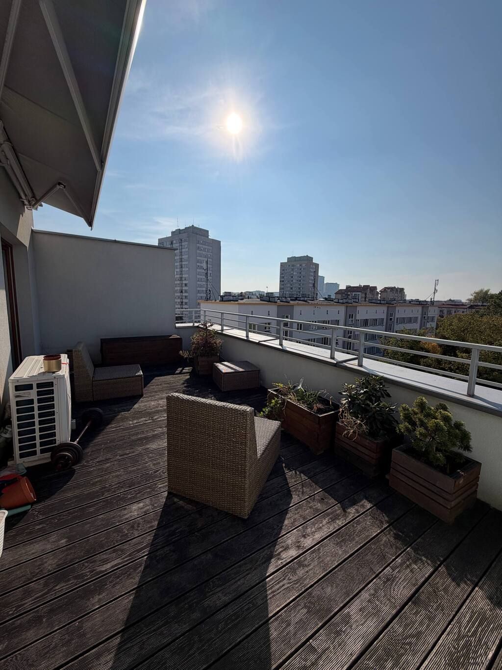 A rooftop terrace with a view of surrounding buildings, a pergola, and outdoor furniture.