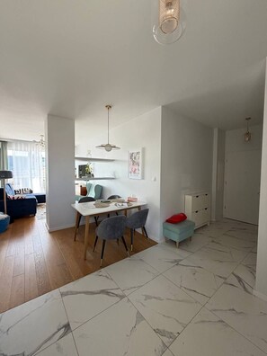 A modern living space with a dining area, a kitchen, and a seating area with a sofa and ottoman. - Lumina 2BR Apt w/ Terrace & Parking (Warszawa)