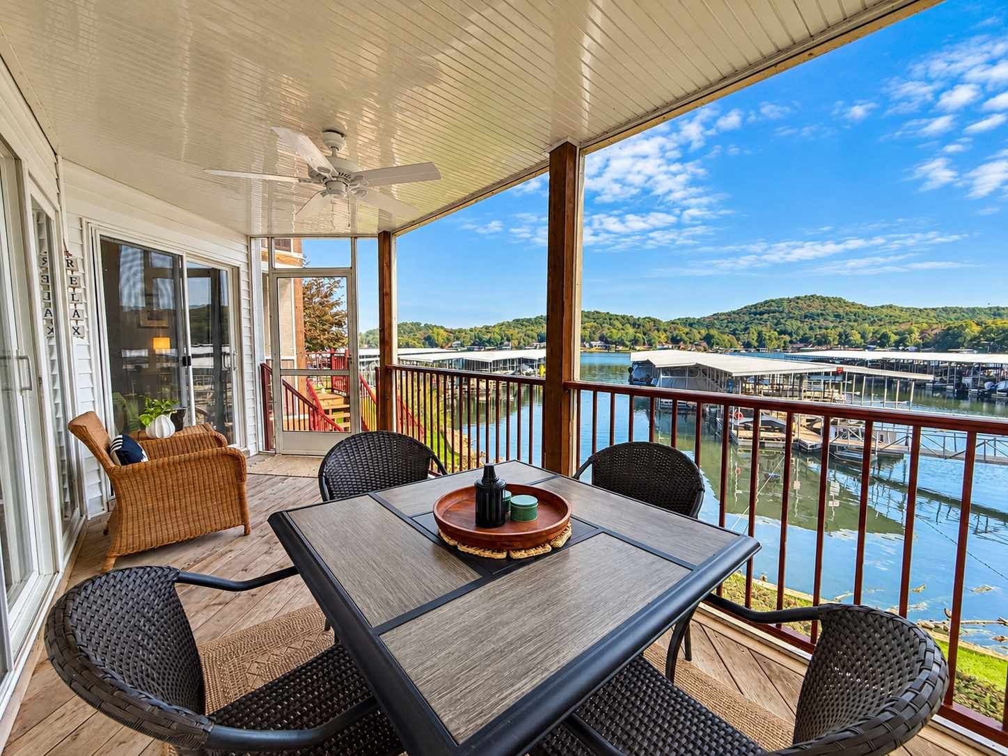 A covered outdoor area with a table and chairs, a ceiling fan, and a view of a body of water and hills.