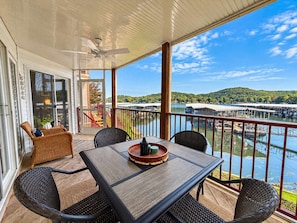 A covered outdoor area with a table and chairs, a ceiling fan, and a view of a body of water and hills. - Big Niangua Getaway - Lake View (Camdenton)