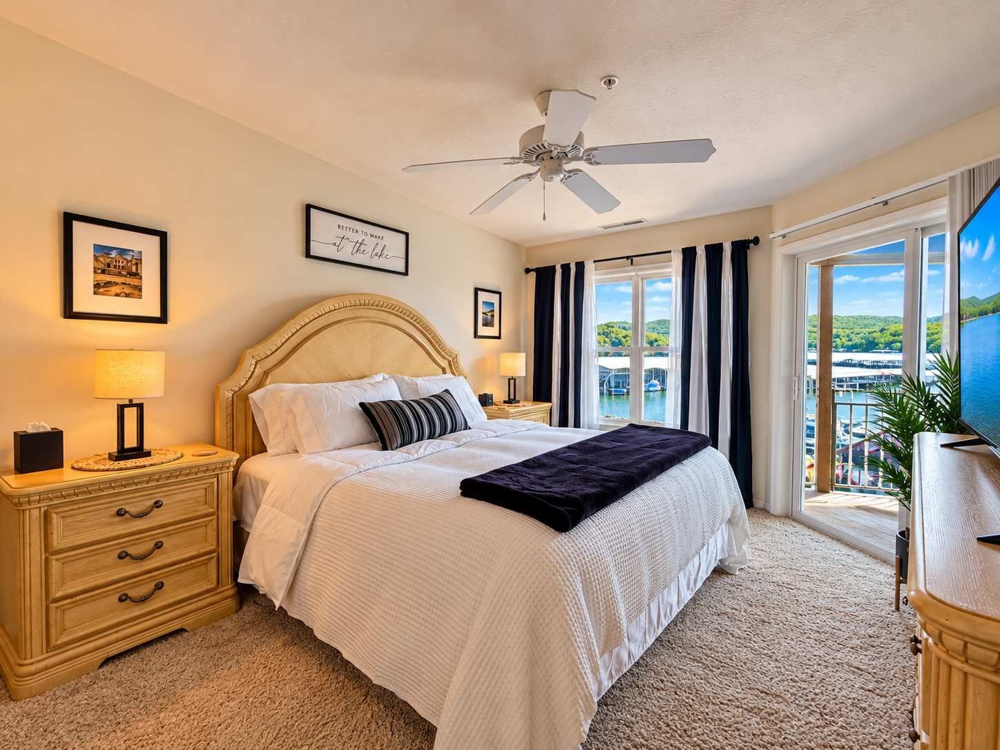 A hotel room with a bed, a nightstand, a lamp, a ceiling fan, a window with curtains, and a TV.