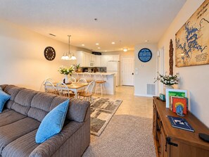 Ein modernes Wohnzimmer mit einer Couch und Sesseln, eine Küche mit weißen Schränken und ein Essbereich mit Tisch und Stühlen.
