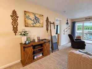 A living room with a map, a wooden console, a chair, and a view of the outdoors. - Big Niangua Getaway - Lake View (Camdenton)