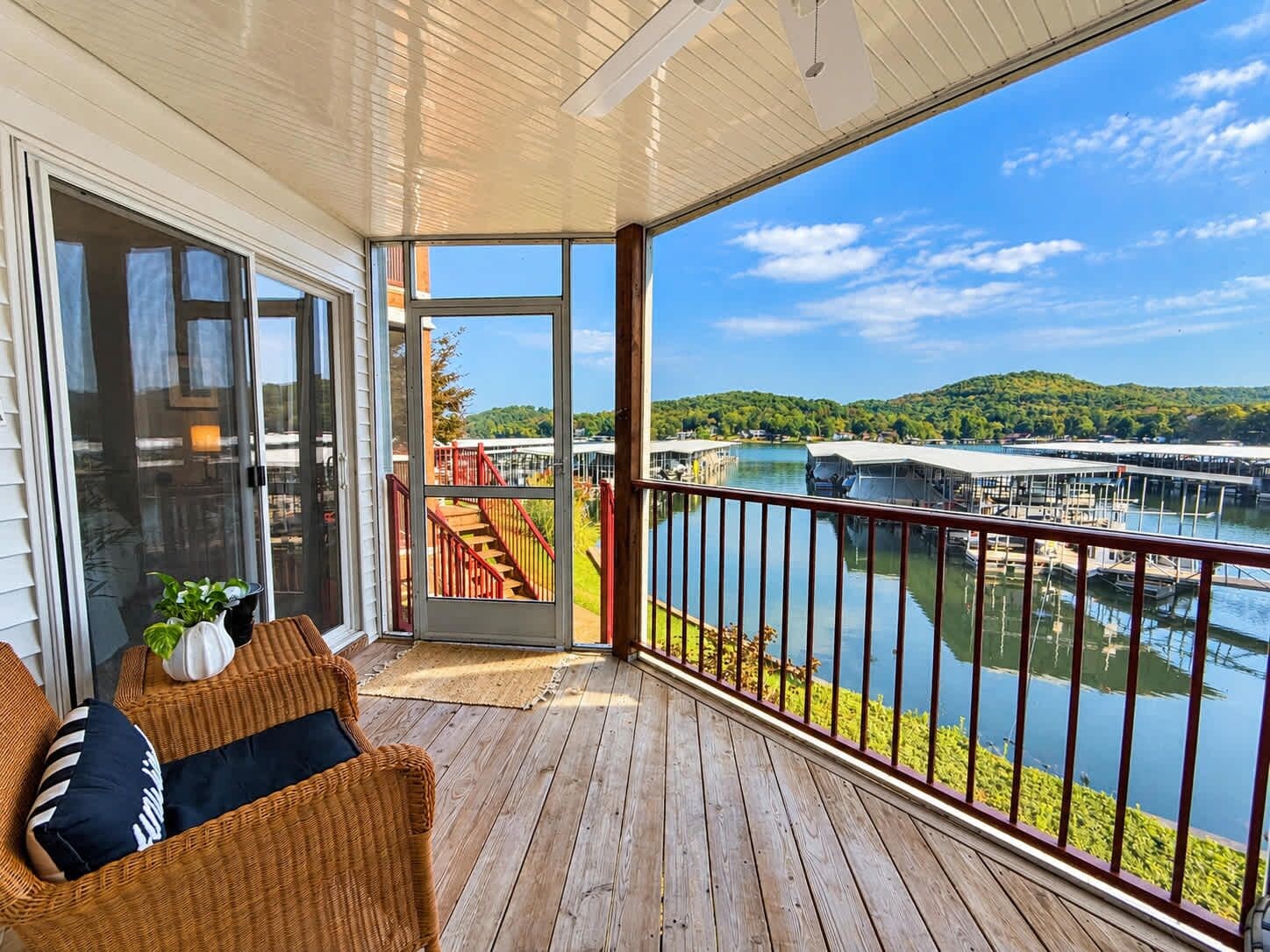 Una terraza de madera con puerta de vidrio que da a un balcón con vista a un lago, con muelles y barcos.