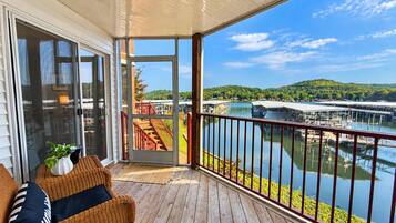 Una terraza de madera con puerta de vidrio que da a un balcón con vista a un lago, con muelles y barcos.