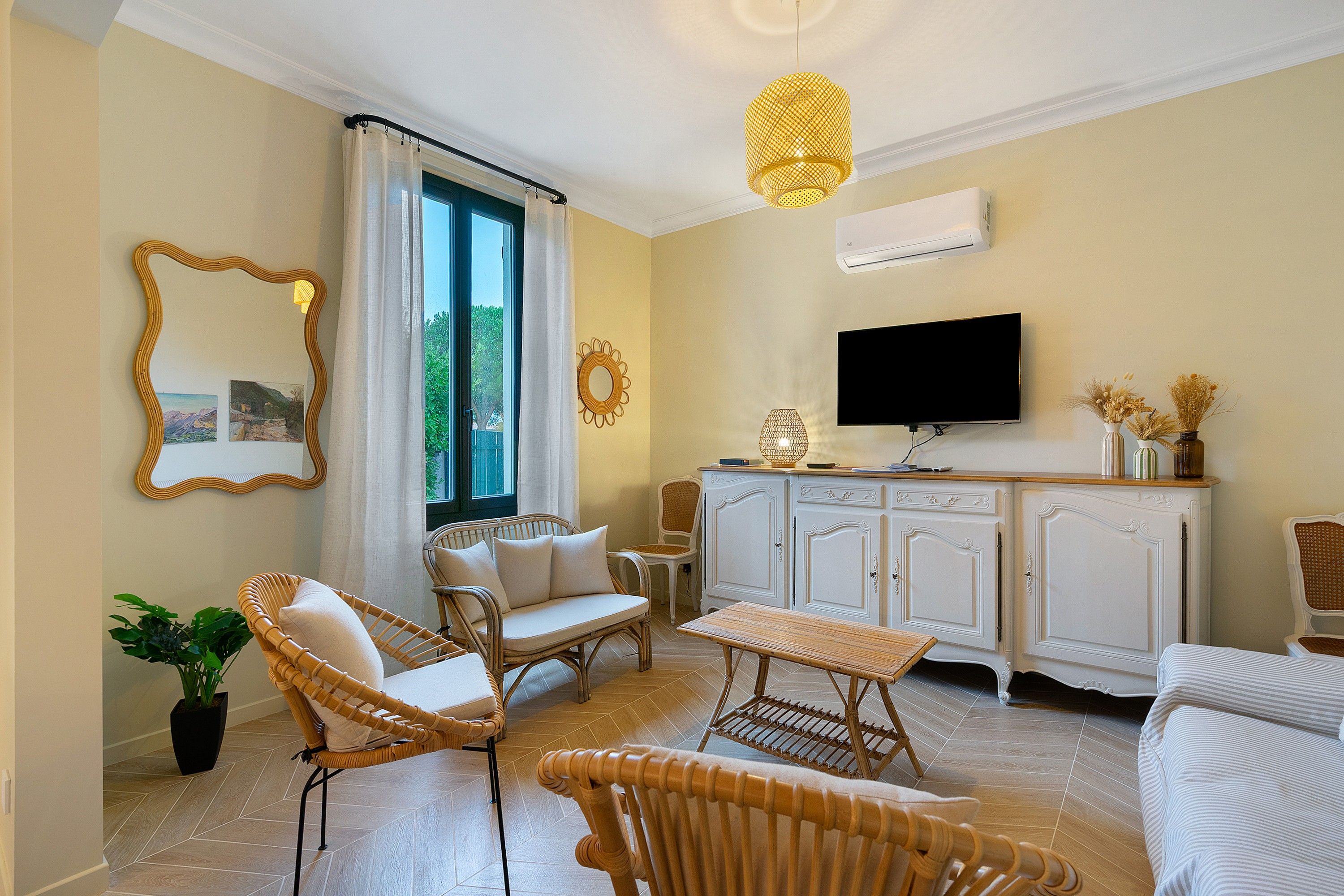 A furnished living room with a television, wicker furniture, and a large window.