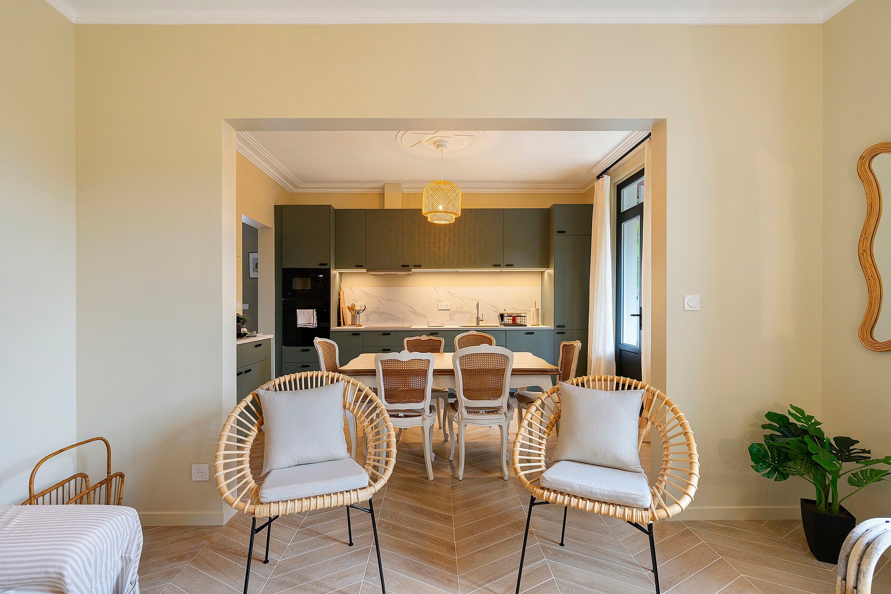 Un comedor con sillas de mimbre, una mesa de mármol y una cocina al fondo.
